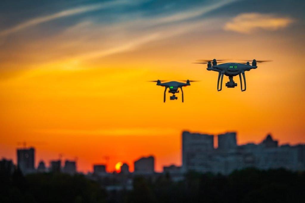 Two drone quad copters with high resolution digital camera flying aerial over spectacular sunset orange sky.